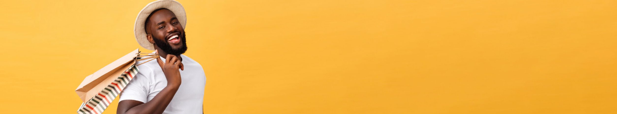 Happy african american man holding shopping bags on yellow background. Holidays concept.